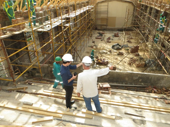 Two men in hard hats pointing at a construction site with scaffolding
